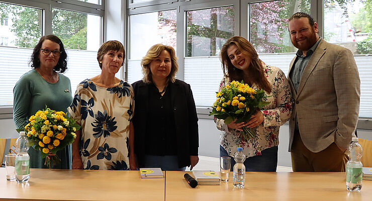 Zwei Frauen mit Blumen, zwei weitere Frauen und ein Mann stehen nebeneinander und lächeln.