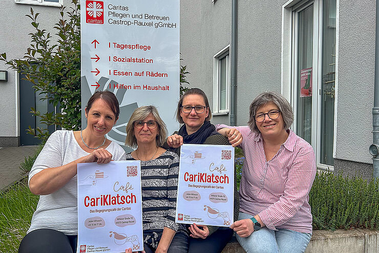 Vier Frauen sitzen nebeneinander und halten Plakate mit der Aufschrift Café Cariklatsch hoch.