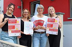 Vier lächelnde Frauen halten Plakate und Bilder in die Kamera.