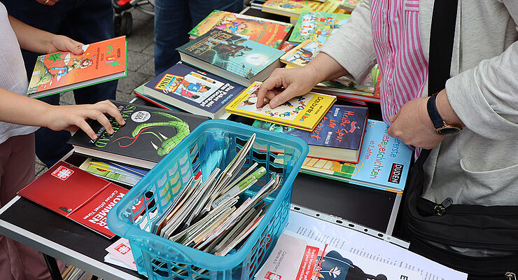 Hände mit Büchern in der Hand und ein Tisch mit vielen Büchern.
