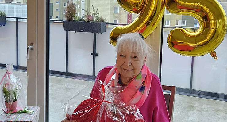 Eine ältere Frau lächelt, im Hintergrund hängt eine große 95.