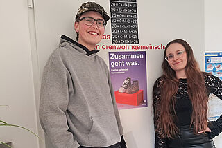 Zwei junge Menschen stehen vor einem Plakat mit der Aufschrift Zusammen geht was.