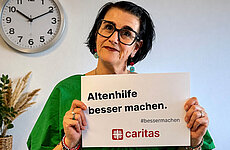 Eine Frau hält ein Schild mit der Aufschrift "Altenhilfe besser machen" in die Kamera.