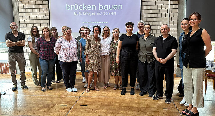 Eine Gruppe Menschen steht nebeneinander vor einer Leinwand mit der Aufschrift "brücken bauen".