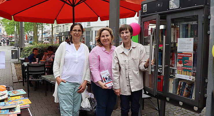 Drei Frauen stehen nebeneinander vor einem Bücherschrank.